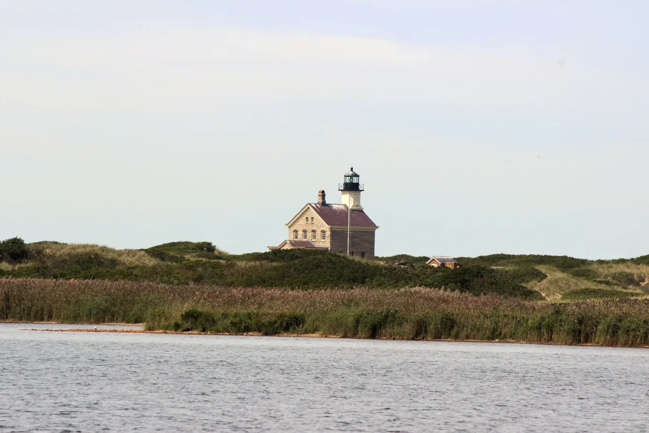 Block Island North Light rises beyond water and coastal vegetation bordering the national wildlife refuge.