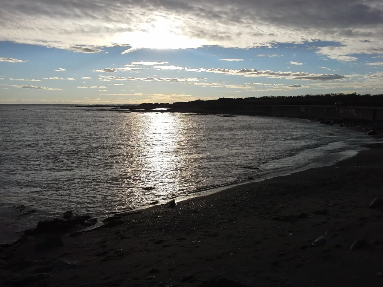 Sunlight breaks through clouds over the curving shoreline at Brenton Point.