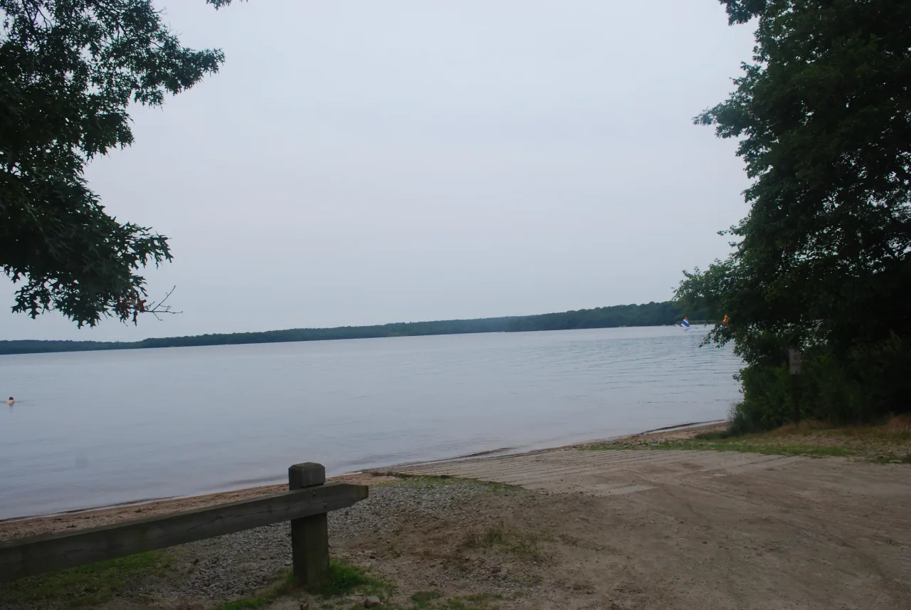 A quiet sandy shore framed by trees on Watchaug Pond.
