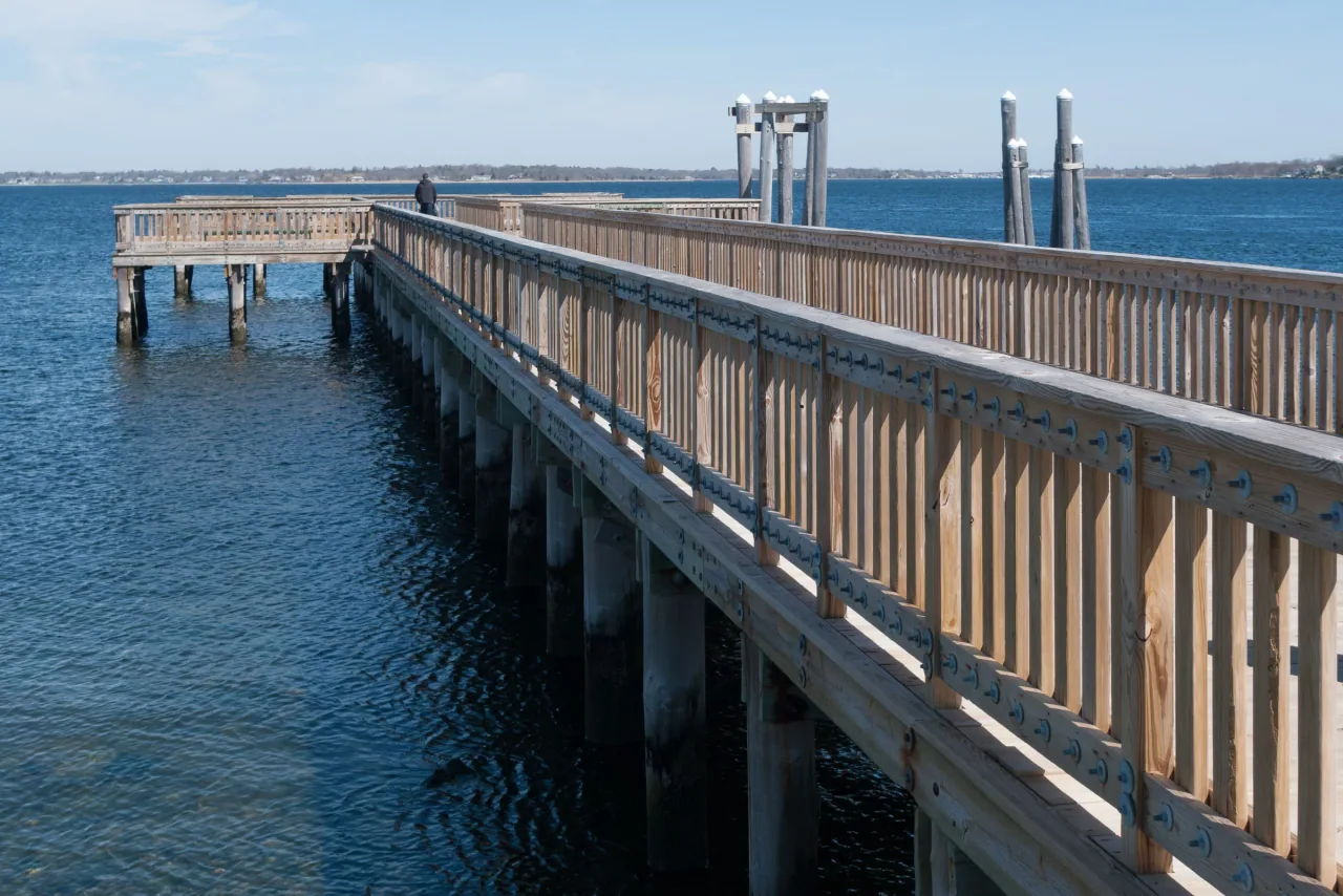 The wooden fishing pier extends over blue water at Colt State Park.