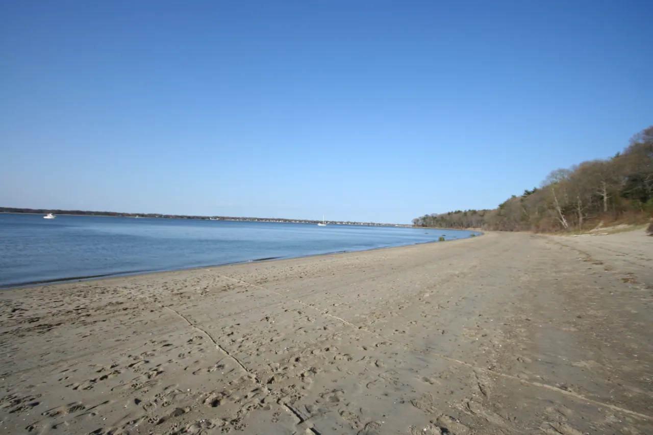 A sandy beach curves along the calm bay at Goddard Memorial State Park.