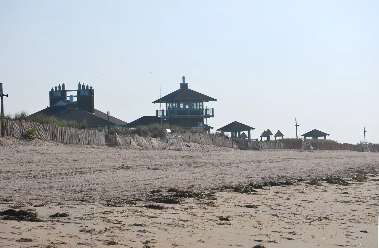 Empty sand, dune fences, lifeguard chairs, and the beachfront pavilion at Misquamicut State Beach.