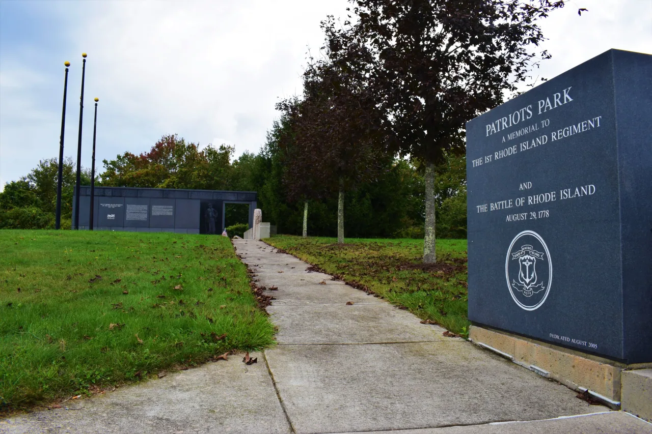 A path across the lawn at Patriots Park leads past its entrance stone to the First Rhode Island Regiment memorial.
