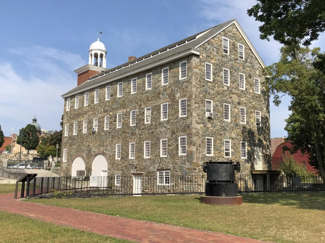 The stone walls and bell tower of Wilkinson Mill under a blue sky in Pawtucket.